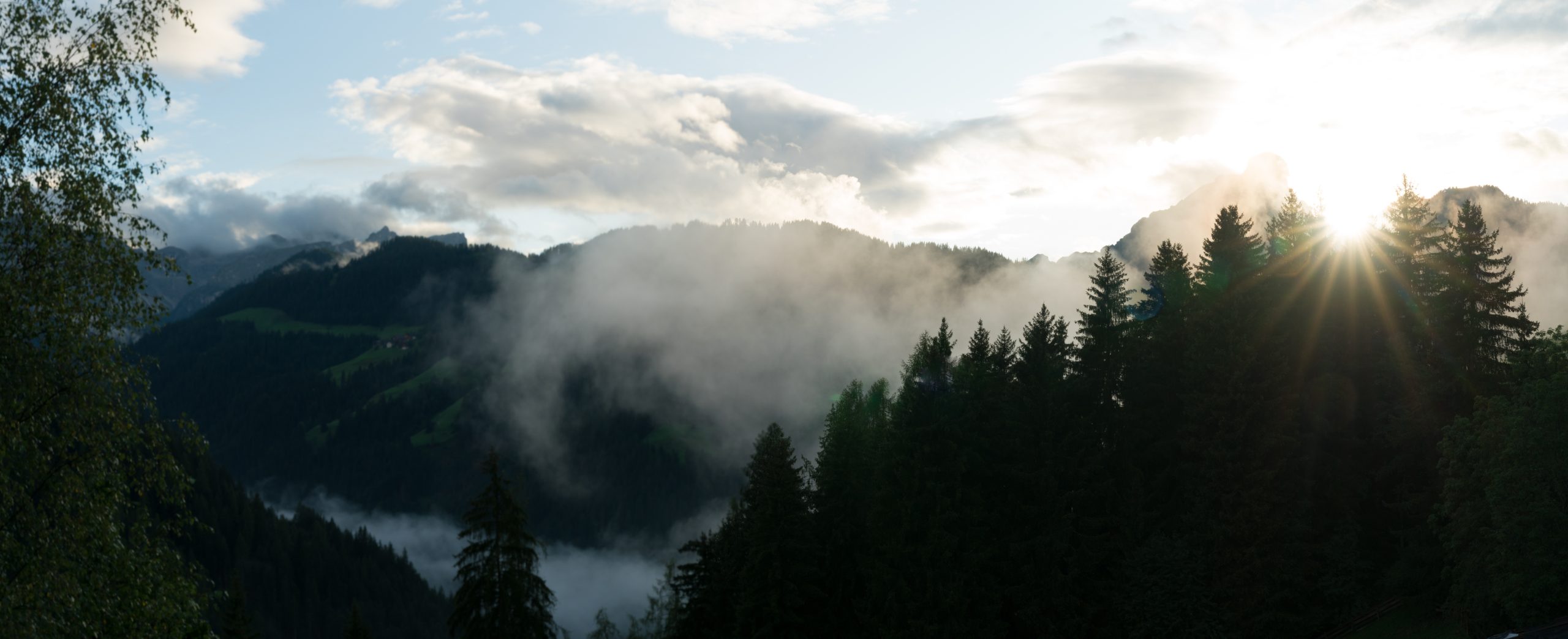 sun shining through fog and clouds after rain in a forest and mountain landscape